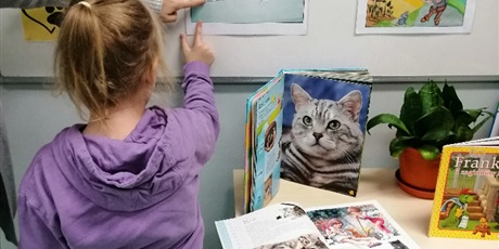 Powiększ grafikę: Dziewczynka pokazuje razem z nauczycielem zdjęcie z bajki "Kot Filemon" przyczepione na tablicy.