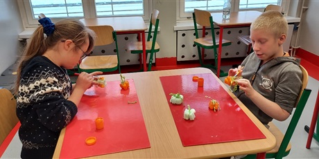 Powiększ grafikę: Dziewczynka i chłopiec malują farbami przy stoliku małe dynie z masy solnej.