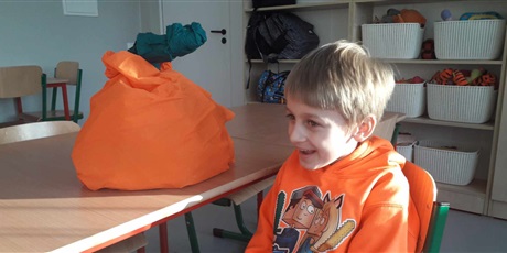 Powiększ grafikę: Chłopiec w pomarańczowej bluzce siedzi obok stolika, na którym leży dynia z papieru.