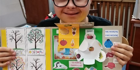 Powiększ grafikę: Chłopiec trzyma wykonaną książkę wyklejoną motywami jesiennymi.