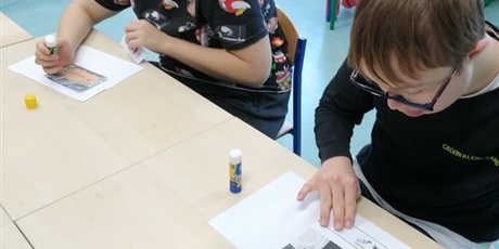 Powiększ grafikę: Dwoje uczniów przykleja na swoich kartkachobrazki i symbole PCS.