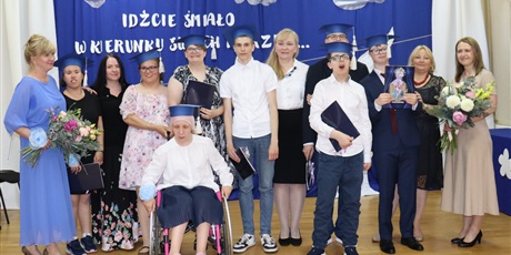 Powiększ grafikę: Zdjęcie grupowe, uczniowie, wychowawcy i dyrektorki stoją na niebieskim tle.