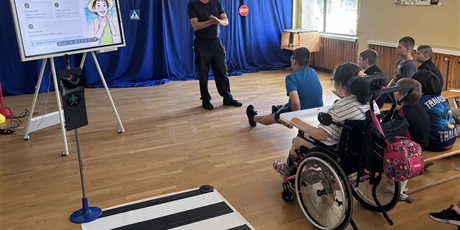 Powiększ grafikę: Uczniowie siedzą na ławkach oglądają prezentację, pielęgniarz stoi przed nimi i mówi.
