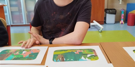 Powiększ grafikę: Chłopiec siedzi przy stoliku, na którym rozłożone są ilustracje.