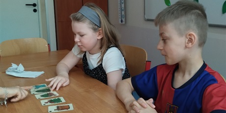 Powiększ grafikę: Dziewczynka i chłopiec siedzą przy stolku, na którym rozłożone są karty z obrazkami.