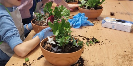 Powiększ grafikę: Uczniowie wraz z nauczycielką sadza rośliny w doniczkach.