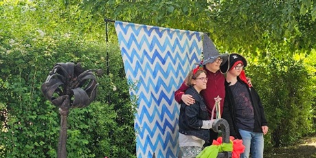 Powiększ grafikę: Trójka uczniów stoi na tle krzewów i tła w niebieskie zygzaki, pozuje do zdjęcia.