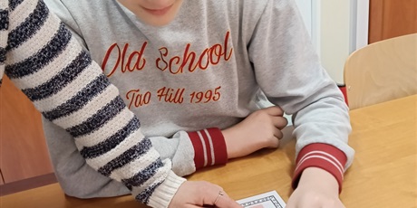 Powiększ grafikę: Chłopiec ogląda kartę, na której jest niebieski kwiat a pod nim paleta kolorów.