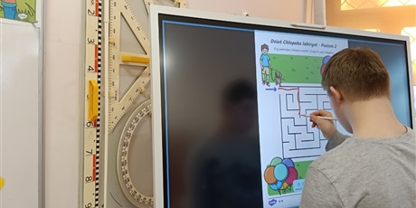 Powiększ grafikę: Chłopiec rysuje drogę przez labirynt na tablicy multimedialnej.