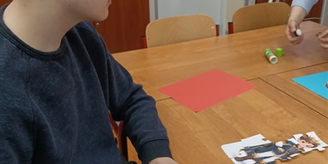 Powiększ grafikę: Chłopiec siedzi przy stole, układa puzzle, na których jest rysunek księcia.