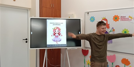 Powiększ grafikę: Chłopiec naśladuje ćwiczenie przedstawione ptrzez księżniczkę na tablicy multimedialnej.