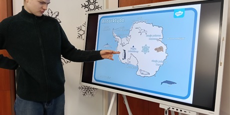Powiększ grafikę: Uczeń stoi przy tablicy multimedialnej i pokazuje pingwina na mapie Antarktydy.