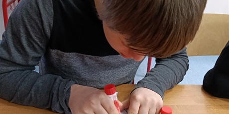 Powiększ grafikę: Uczeń siedzi przy stoliku, smaruje klejem kartkę.