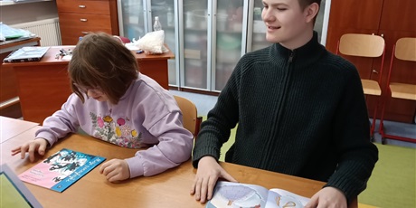 Powiększ grafikę: Chłopiec i dziewczynka siedzą przy stoliku, oglądają książki o pingwinach.