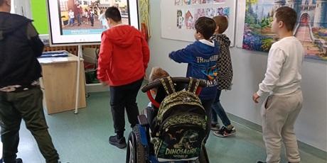 Powiększ grafikę: Uczniowie tańczą na środku sali naśladując ruchy postaci prezentowanych na tablicy.