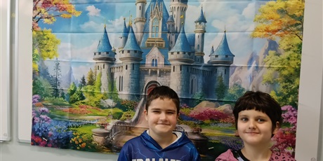 Powiększ grafikę: Dwóch chłopców stoją na tle plakatu z baśniowym zamkiem.