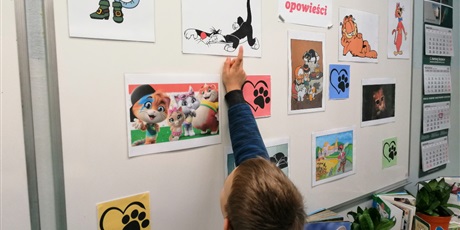 Powiększ grafikę: Chłopiec pokazuje na tablicy ze zdjęciami kotów bohaterów bajek jedno zdjęcie.