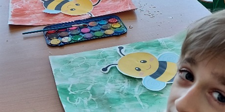 Powiększ grafikę: Dwóch uczniów siedzi przy stoliku na którym leżą farby pomalowane dwie kartki papieru i dwie papierowe pszczoły.