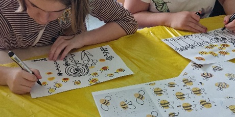 Powiększ grafikę: Uczennice siedzą przy stoliku, malują czarnym flamastrem kwiaty na białej kartce.