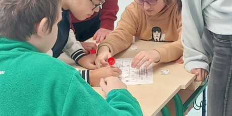 Powiększ grafikę: Uczniowie dookoła stolika układają puzzle matematyczne.