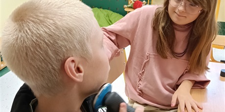 Powiększ grafikę: Chłopiec i dzewczynka siedza przy stoliku, chłopiec trzyma golarkę, udaje, że się goli. Dziewczynka przygląda mu się.