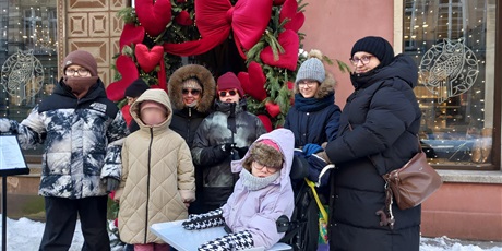 Powiększ grafikę: Uczniowie i opiekunowie stoją grupą na tle dekoracji z sercami.