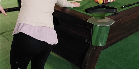 Powiększ grafikę: Dziewczynka uderza kijem w kule bilardowe.