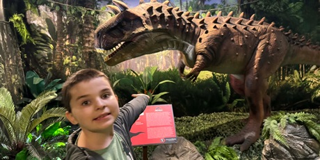 Powiększ grafikę: Chłopiec wskazuje figurę dinzaura.