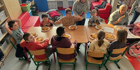 Powiększ grafikę: Uczniowie siedzą przy stole, przed każdym stoi talerz z pizzą.