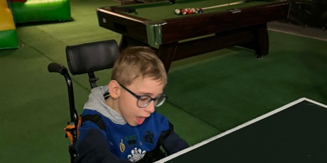 Powiększ grafikę: Chłopiec na wózku odbija piłeczkę na stole do ping-ponga.