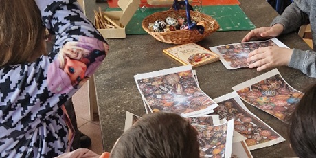 Powiększ grafikę: Uczniowie przy stole oglądają zdjęcia z różnorodnymi pisankami.
