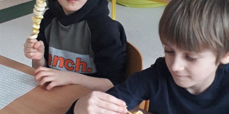 Powiększ grafikę: Dwóch chłopców siedzi przy stoliku. Nakładają na patyczek kawałki różnych owoców.