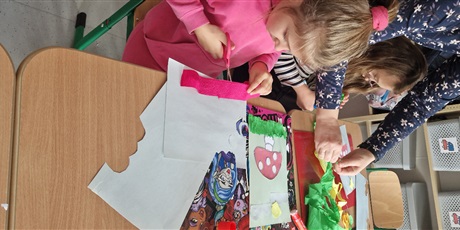 Powiększ grafikę: Dwie dziewczynki przy stoliku, przed nimi kartki, wycinają kolorową bibułę.