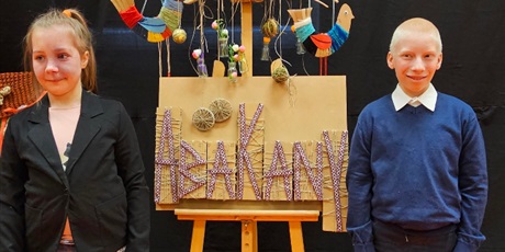 Powiększ grafikę: Dziewczynka i chłopiec stoją prz leżącym na sztalugach napisie "Abakany".