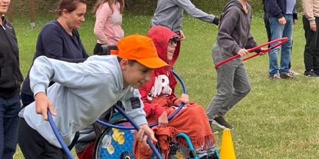 Powiększ grafikę: Uczniowie na boisku szkolnym, zawody sportowe - wysćigi z kolami hula-hop.
