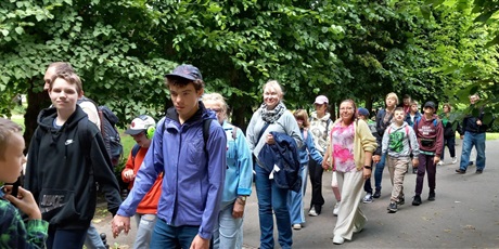 Powiększ grafikę: Grupa uczniów wraz zopiekunami idzie parami po deptaku wśród drzew.