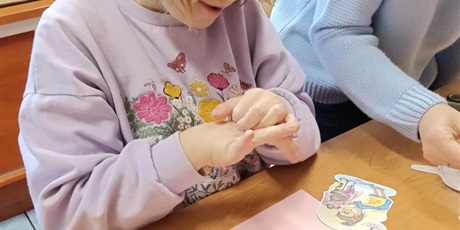 Powiększ grafikę: Dziewczynka z nauczycielką wybiera obrazk leżące na stole.