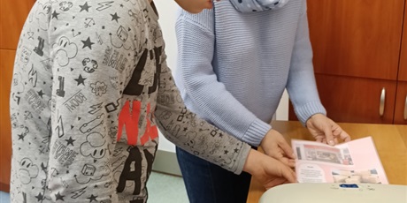 Powiększ grafikę: Chłopiec z nauczycielką laminują kartkę.