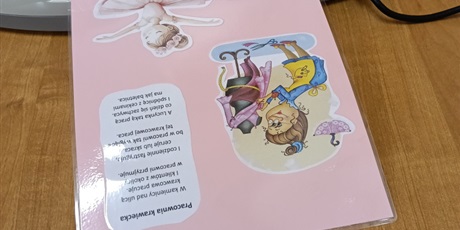 Powiększ grafikę: Kartka z wierszykiem i obrazkami zalaminowana leży na stole.