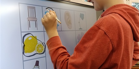 Powiększ grafikę: Chłopiec zaznaca obrazki na tablicy multimedialnej.