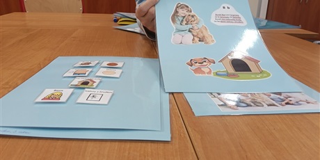 Powiększ grafikę: Na stole leżą karty z książki z obrazkami, symbolami PCS i tekstem.