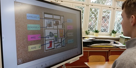 Powiększ grafikę: Chłopiec stoi przy tablicy multimedialnej, na której wyświetlane jest zadanie.