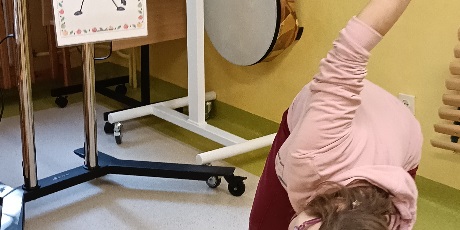 Powiększ grafikę: Dziewczynka wykonuje skłon zgodnie z instrukcją na obrazku.