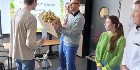 Powiększ grafikę: Chłopiec stoi naprzeciwko mężczyzny, który trzyma zapakowane pudełko.
