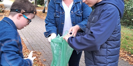 Powiększ grafikę: Kobieta i chłopiec trzymają zielony worek na śmieci, drugi chłopiec trzyma plastikowy worek.