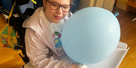 Powiększ grafikę: Dziewczynka na wózku trzyma niebieskiego balona.