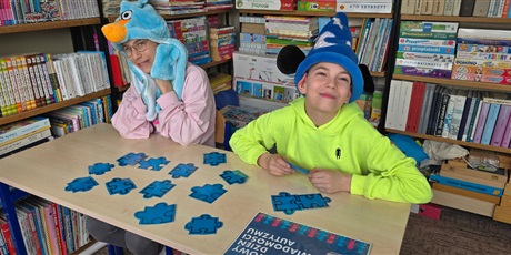 Powiększ grafikę: Chłopiec i dziewczynka w wesołych niebieskich czapkach siedzą przy stoliku, na którym leżą niebieskie puzzle.