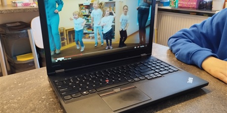Powiększ grafikę: Na stole stoi laptop, na ekranie widać dzieci.