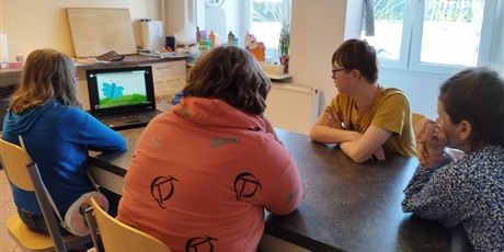 Powiększ grafikę: Czworo uczniów siedzi przy stole, na którym stoi otwarty laptop, oglądają film.