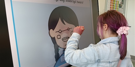 Powiększ grafikę: Dziewczynka dorysowuje elementy twarzy postaci na tablicy multimedialnej.